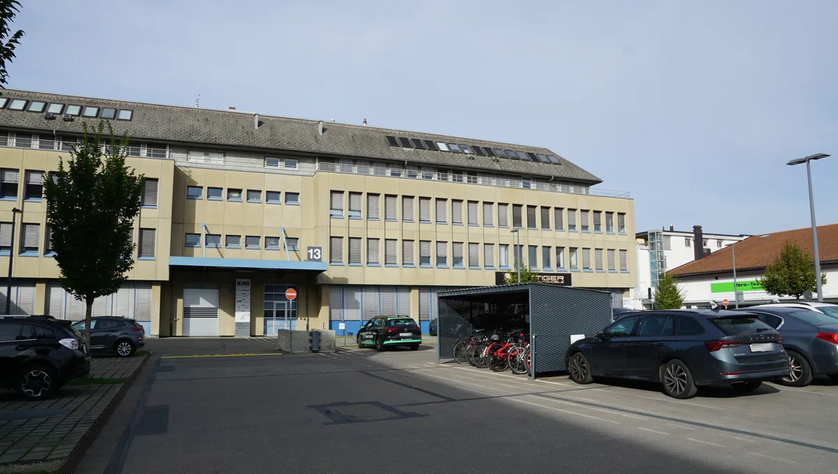 Dieses Haus wird zum Wohnhaus. Die bestehende Bausubstanz wird dafür genutzt. Man sieht ein Gebäude und einen Parkplatz.